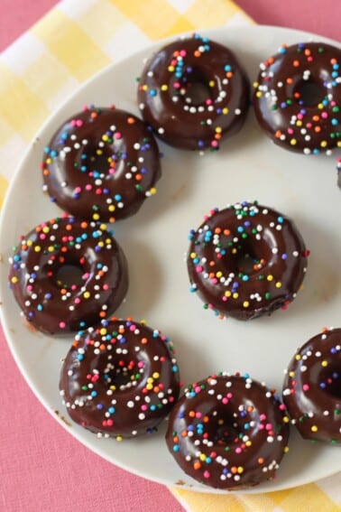 Half a plate full of Mini Chocolate Doughnuts on a yellow, pink and white surface.