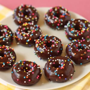 Close up of a plate full of Mini Chocolate Doughnuts on a pink, white and yellow background.