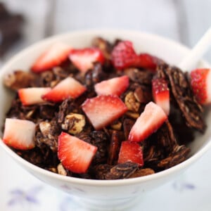 A bowl of Chocolate Granola with chopped strawberries on top.