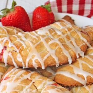 Strawberry Hand Pies stacked on a white plate by a checkered napkin and strawberries.