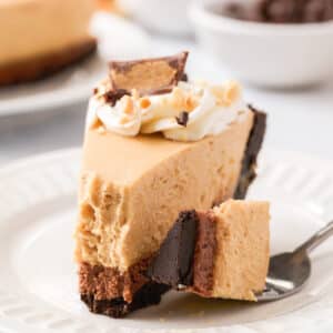 Close up of a slice of Peanut Butter Chocolate Pie on a white plate with a fork holding a bite to show the texture of the pie.