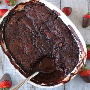 Top view of a Chocolate Strawberry Pudding Cake with a spoon inserted to show chocolate pudding sauce.