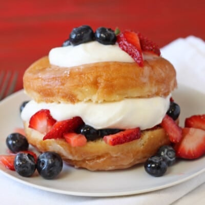 Close up of a Doughnut Strawberry Shortcake topped with fruit on a white plate.