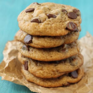 A stack of Peanut Butter Banana Chocolate Chip Cookies on a piece of parchment with a teal background.