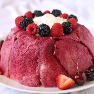 Close up of a Summer Pudding on a white plate next to fresh fruit.