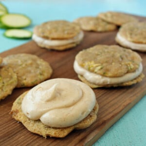 Several Zucchini Whoopie Pies on a wooden cutting board with the top off the front cookie to show the frosting.