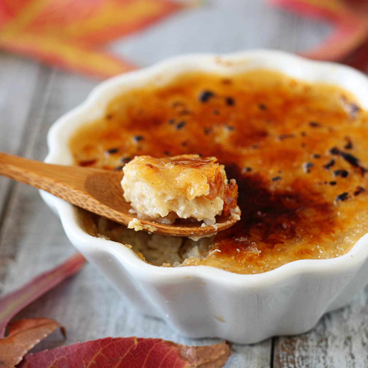 Close up of Rice Pudding Brulee in a white ramekin and a small wooden spoon lifting out a bite.