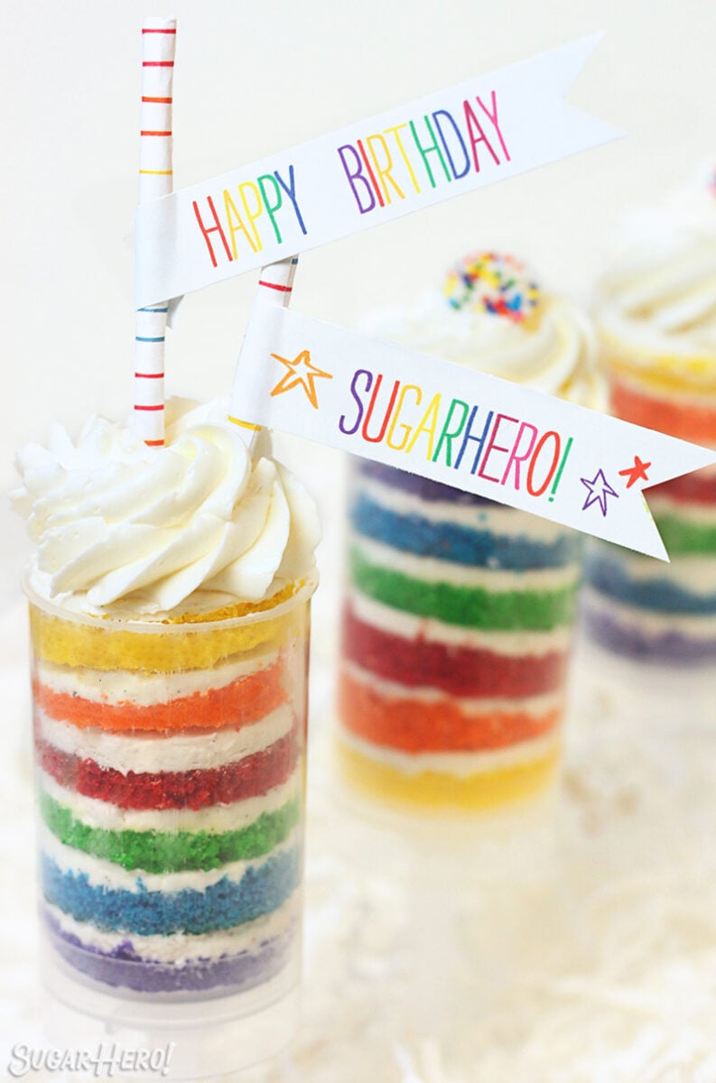 Rainbow Cake Push-Up Pops | SugarHero.com Rainbow Cake Push-Up Pops in front of a white surface with "Happy Birthday SugarHero" banners sticking out of the top.