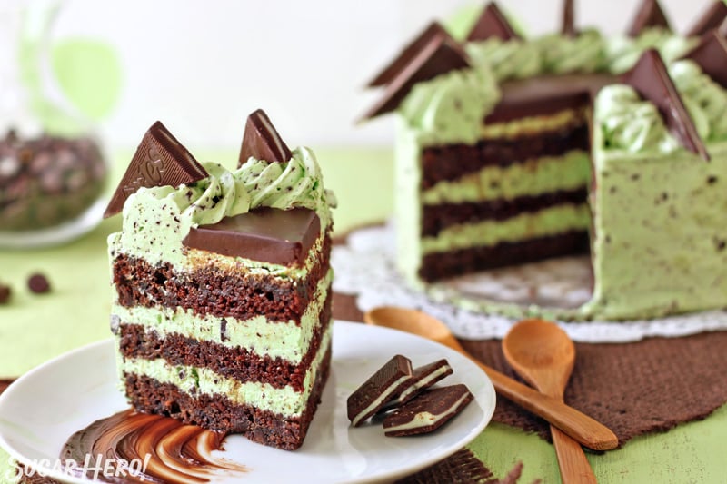 Slice of mint chocolate chip cake on a white plate with a smear of chocolate and the cut cake in the background