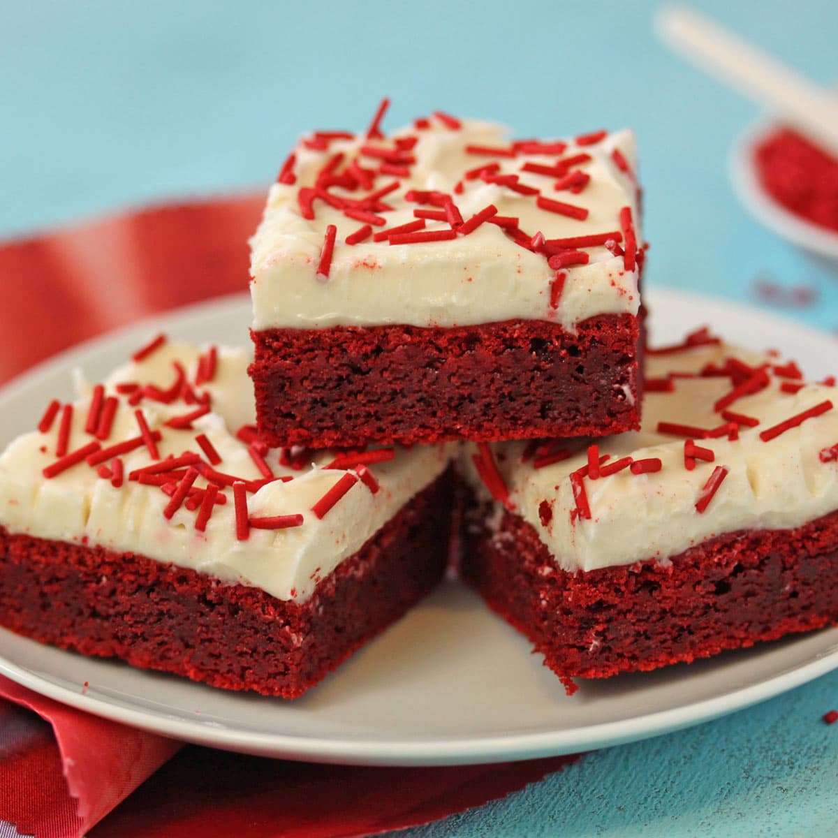 3 Red Velvet Bars on a white plate on a teal surface.