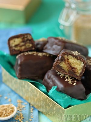 A pile of Chocolate-Dipped Pound Cake squares in a gold box with teal tissue paper.