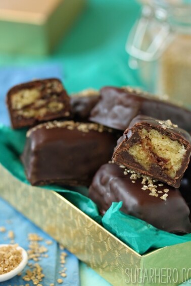 A pile of Chocolate-Dipped Pound Cake squares in a gold box with teal tissue paper.