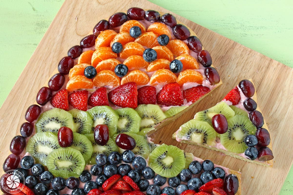 Easter Egg Fruit Pizza on a wooden cutting board with a slice removed