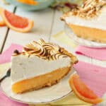 A slice of Grapefruit Meringue Pie on a dessert plate next to a slice of grapefruit.