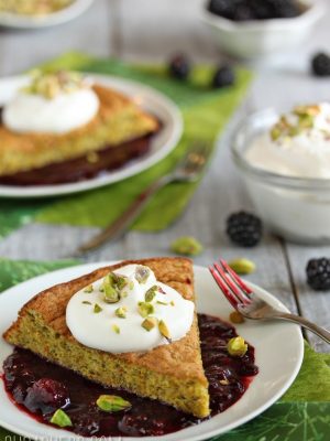 A slice of Pistachio Cake with Blackberry Sauce on a white plate.