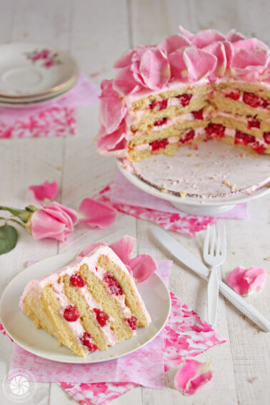 Slice of Raspberry-Rose Cake on a white plate with full cake in the background.