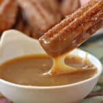 A hand dipping a churro into dulce de leche sauce.