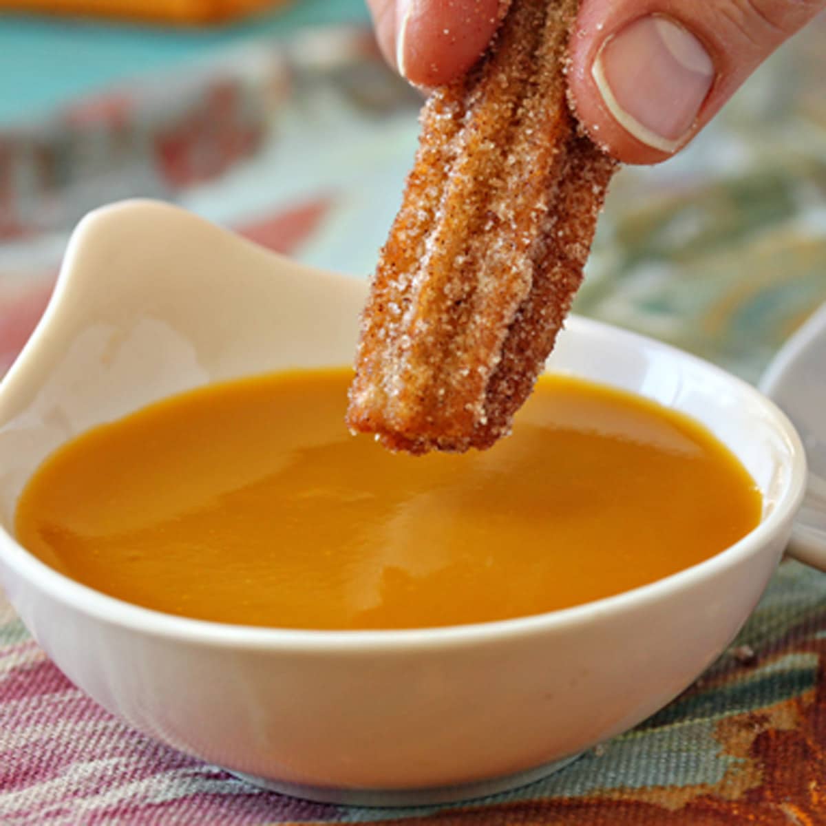 A hand dipping a churro into mango sauce.