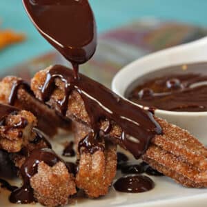 A pile of churros being drizzled with spicy chocolate sauce.