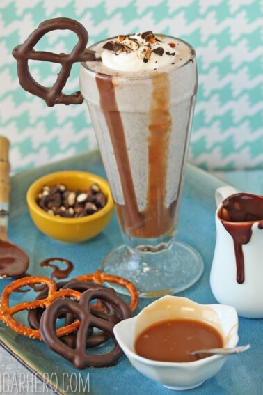 Chocolate Covered Pretzel Milkshake on a tray next to pretzels and dessert sauces.