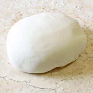 A disc of white homemade fondant on a marble surface.