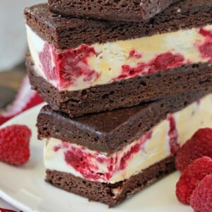 2 Brownie Raspberry Swirl Ice Cream Sandwiches stacked on top of each other on a white plate next to fresh raspberries.