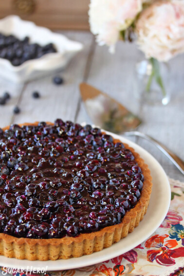Blueberry Coconut Tart on a white round plate, set on a floral napkin with flowers and fresh blueberries in the background.