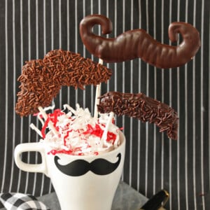 A mustache mug holding 3 Chocolate Mustache Pops.