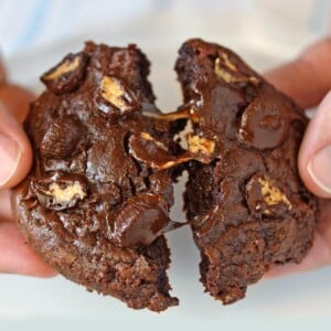 A hand pulling apart a Gooey Chocolate Peanut Butter Cup Cookie to show center.