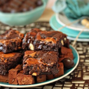 A stack of sliced Triple Chocolate Rocky Road Brownies on a teal plate next to chocolate marshmallows and chocolate-covered almonds.