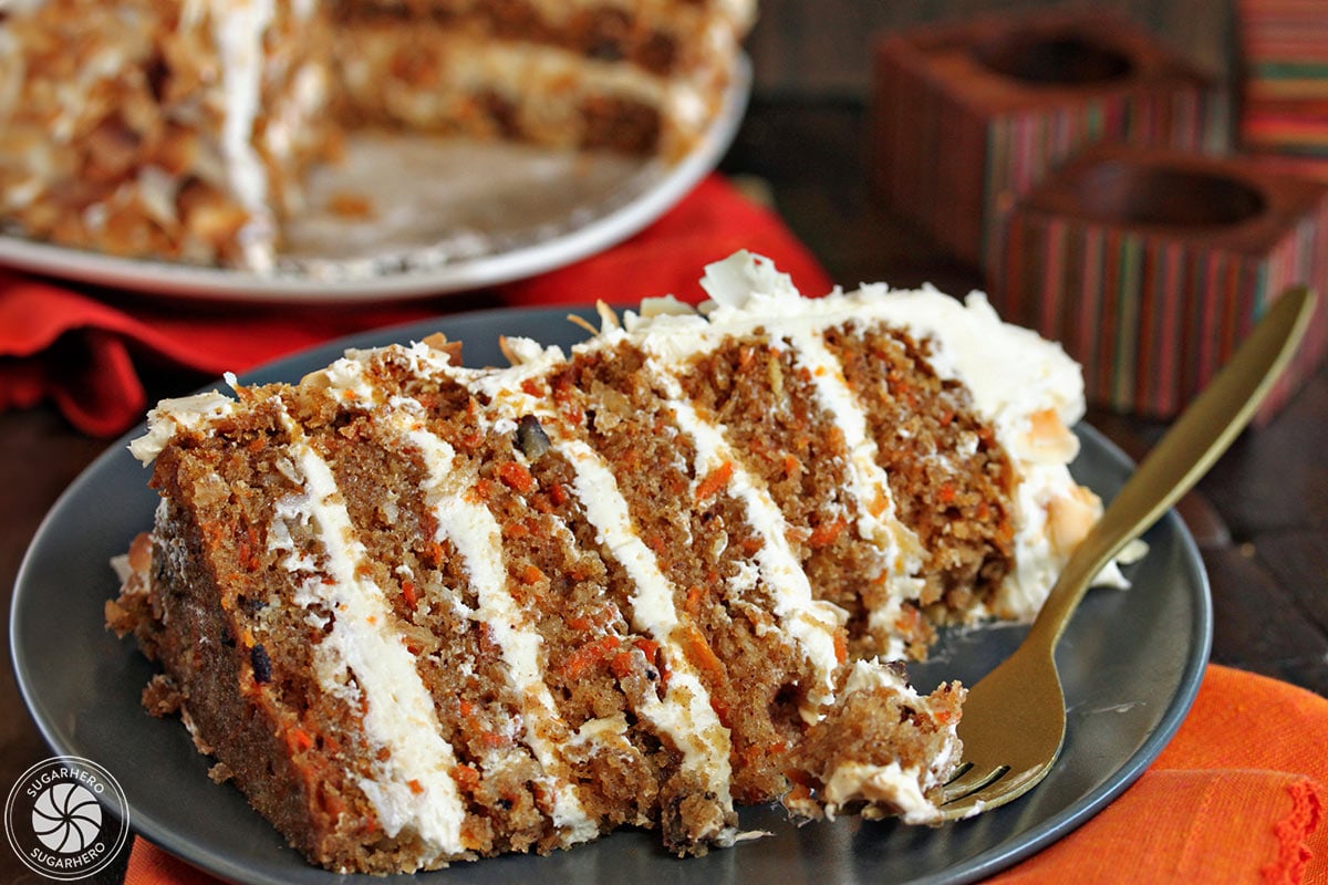 A slice of Carrot Cake with Coconut Cream Cheese Buttercream on a gray plate with a golden fork holding a bite.