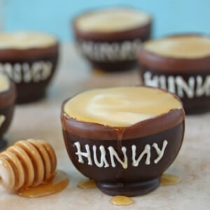 Close up of a Hunny Pot next to a wooden honey spoon.