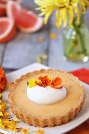 Close up of a Grapefruit Tart on a white plate next to flowers.