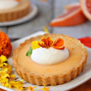 Close up of a Grapefruit Tart on a white plate next to flowers.