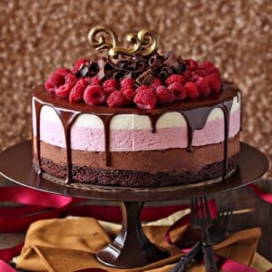 Chocolate Raspberry Mousse Cake topped with raspberries and chocolate curls on a brown cake stand.