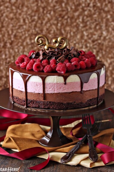 Chocolate Raspberry Mousse Cake topped with raspberries and chocolate curls on a brown cake stand.