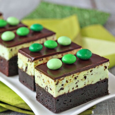 Group of Mint Chocolate Chip Mousse Brownies lined up on a white platter with green linens underneath.