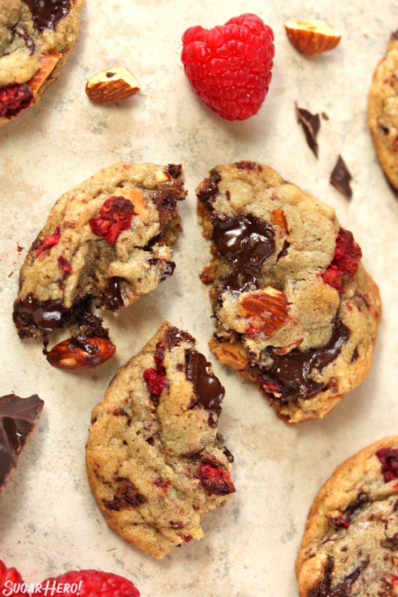 Raspberry Almond Chocolate Chunk Cookies - overhead shot of a cookie broken up on a cutting board | From SugarHero.com