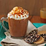 A cup of Salted Caramel Hot Chocolate on a napkin next to cookies.