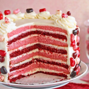 Layer cake with several slices taken out, showing pink and red cake layers with cream cheese frosting.