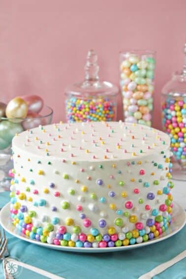 A polka dot cake covered in pastel Sixlets on a blue placemat.