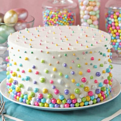 Layer cake covered with white buttercream and colored sprinkles.