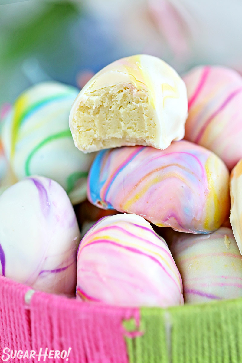 Close-up of white chocolate truffle with a bite taken out of it, on a pile of Marbled Easter Egg Truffles.