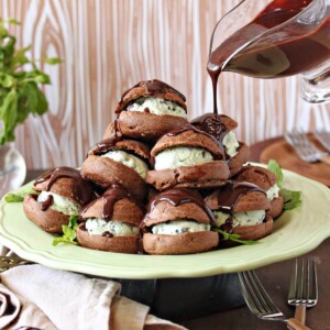 A stack of Chocolate Profiteroles with Fresh Mint Chip Ice Cream on a light green plate with chocolate sauce being poured on top.