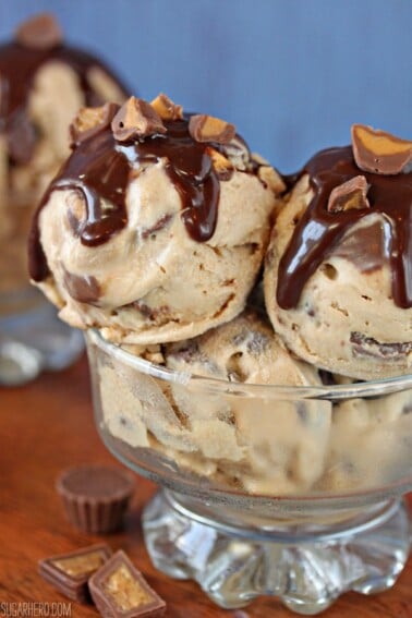 Several large scoops of Peanut Butter Cup Ice Cream in a glass dessert bowl covered with chocolate sauce and chopped peanut butter cups.