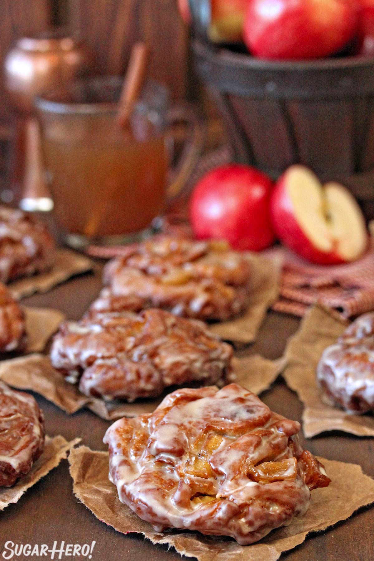 Apple Cider Fritters cooling on brown paper with cider and apples in the background.