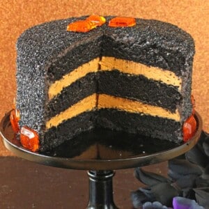 Devil's Food Cake with Pumpkin Butterscotch Frosting on a black cake stand with pieces removed to show interior.