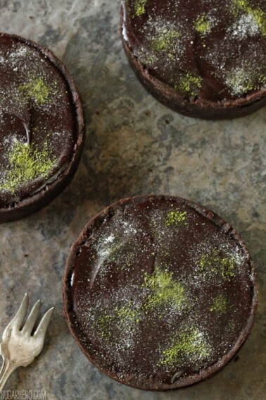 3 Matcha Chocolate Tarts on a marble countertop next to a silver fork.