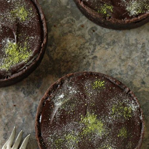 3 Matcha Chocolate Tarts on a marble countertop next to a silver fork.