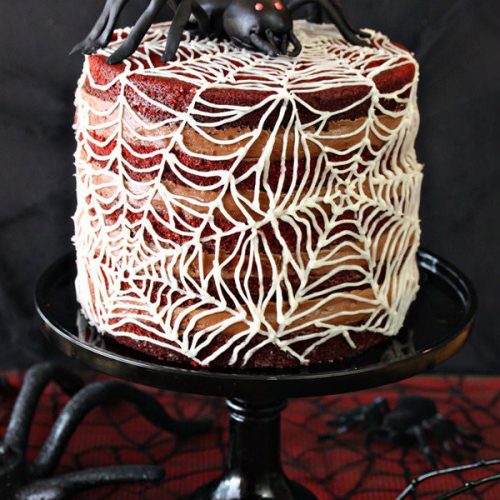Spiderweb Naked Red Velvet Cake on a black cake stand on a black and red table.
